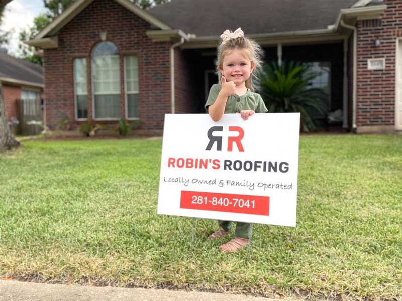 Company owner Adam Robin's daughter giving the thumbs-up behind a Robin's Roofing sign placed in front of a home the company recently worked on